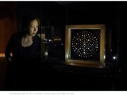 Sotheby’s Withdraws $13 Million Auction After India Reclaims Sacred Buddha Relics A woman observing a glowing star-like light display in a dark room.